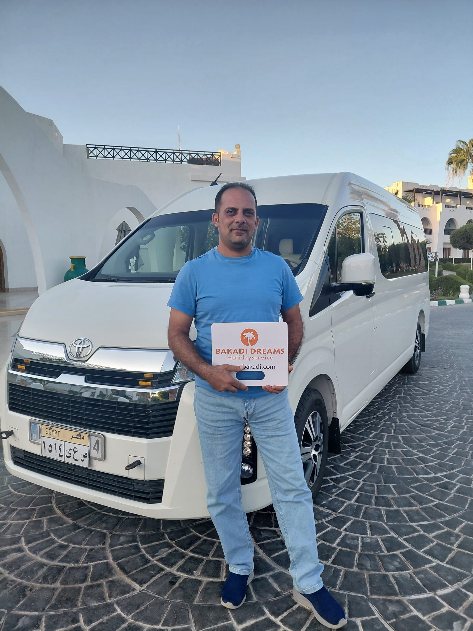 Flughafentransfer Hurghada: Bakadi Dreams Fahrer mit weißem Toyota Hiace Minibus und Namensschild zur Abholung